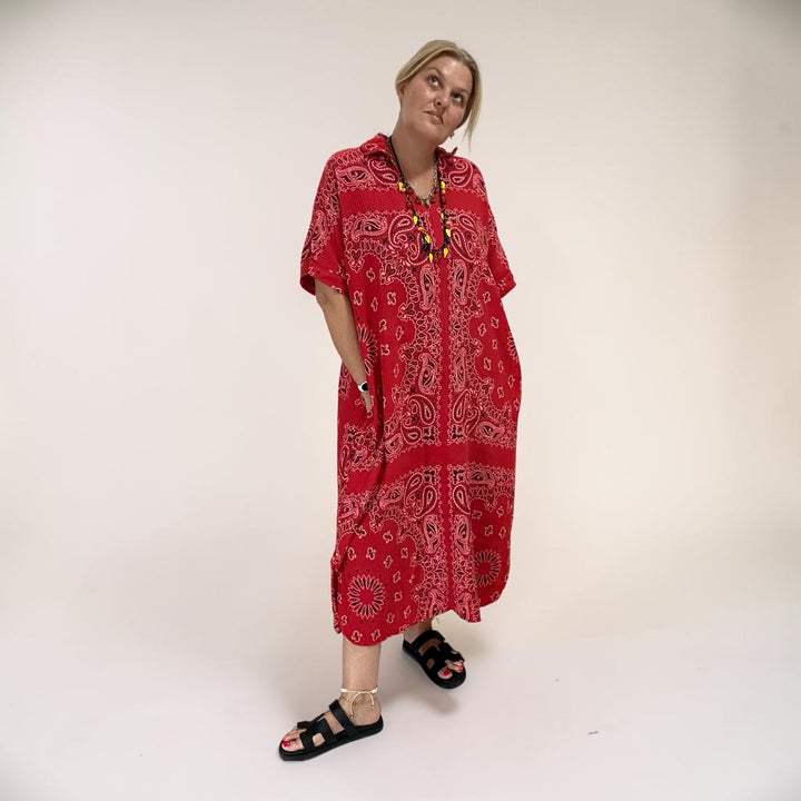 A woman modeling a red and white paisley bandana kaftan cotton gauze dress with black slide sandals